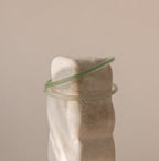 Two thin jade bangles in soft translucent green tones placed on a stone display.