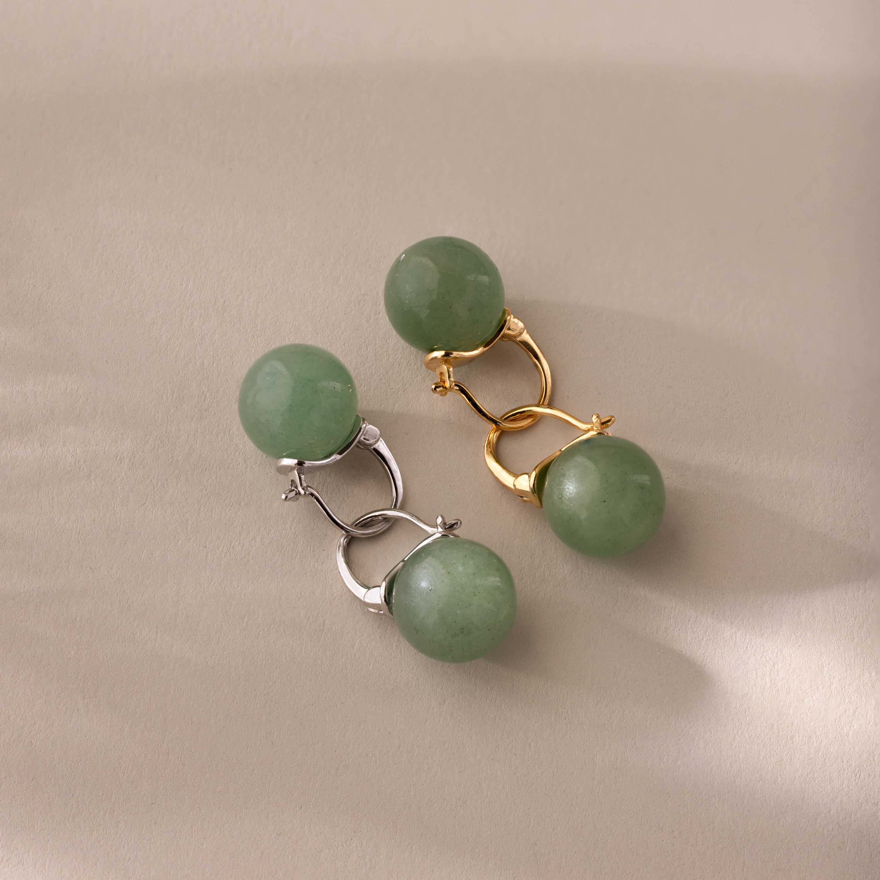 Close-up of two pairs of Jade Dome Drop Earrings in gold and silver, each featuring rounded green gemstones on dainty hoops.