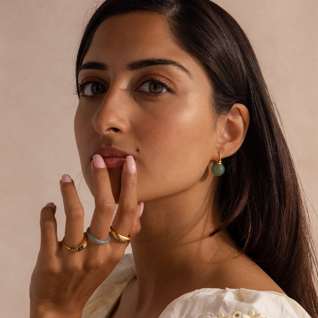 Model wearing gold Jade Dome Drop Earrings featuring rounded green gemstones on dainty hoops, styled with multiple gold rings.
