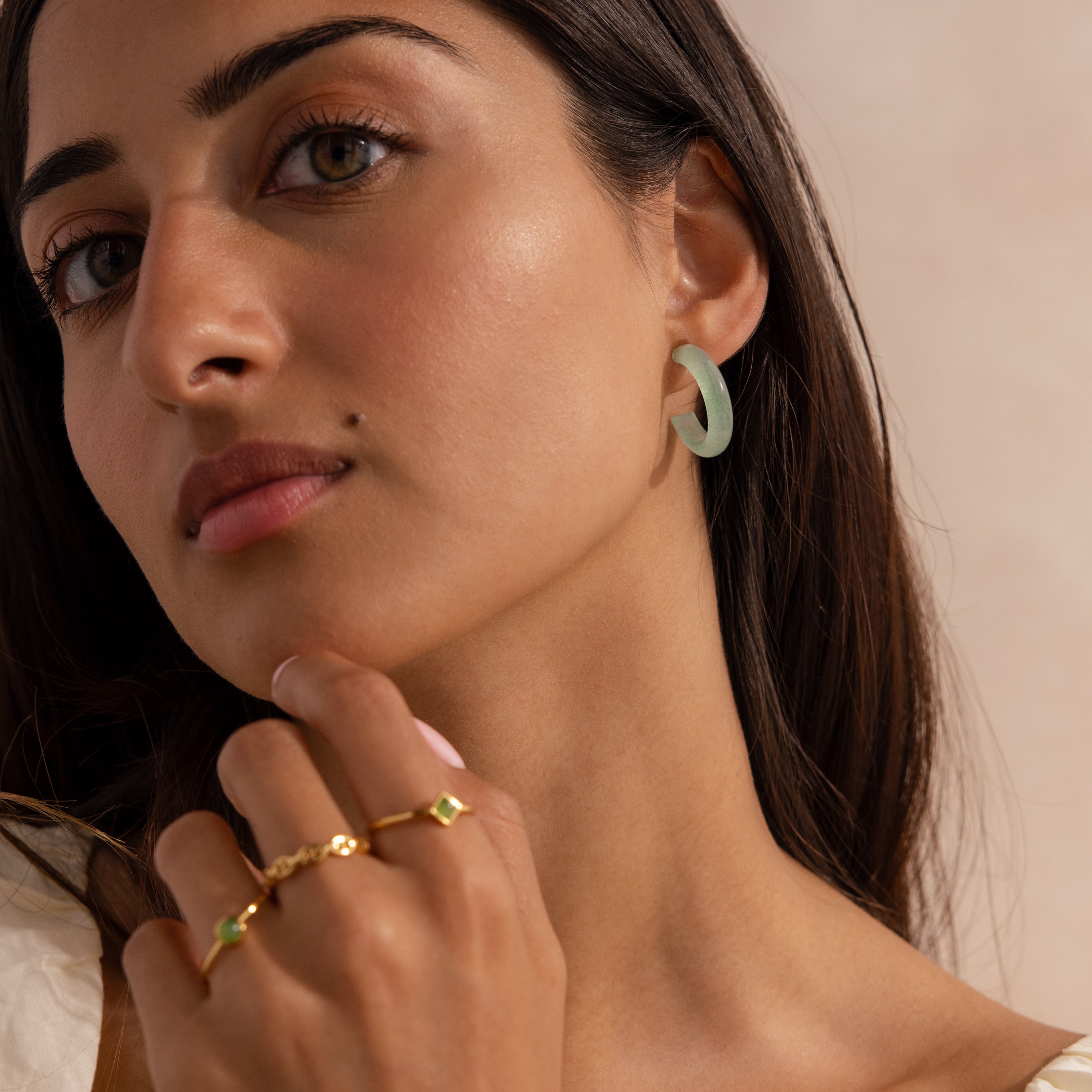 Model wearing Jade Hoop Earrings, featuring a chunky hoop design with a soft green natural jade gemstone, styled with multiple gold rings.