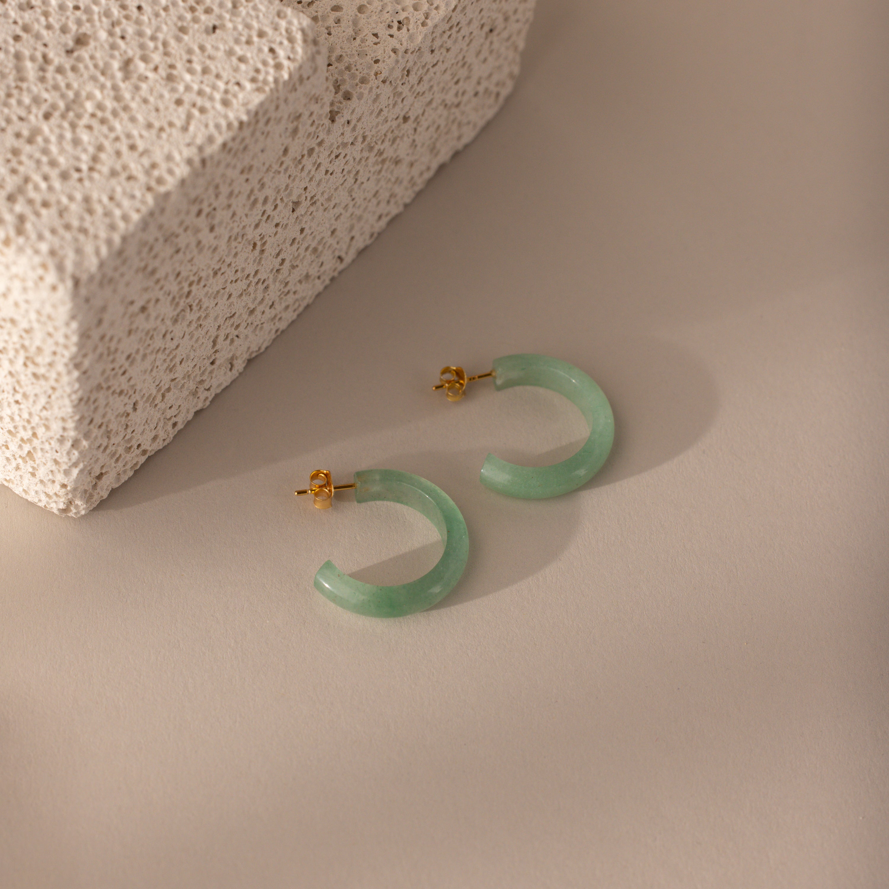 Flat-lay of Jade Hoop Earrings in gold, featuring a chunky hoop design with green jade gemstone on a butterfly back closure.