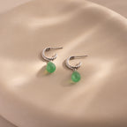 Twisted silver hoops with green jade drops elegantly hanging from a white ceramic vase.