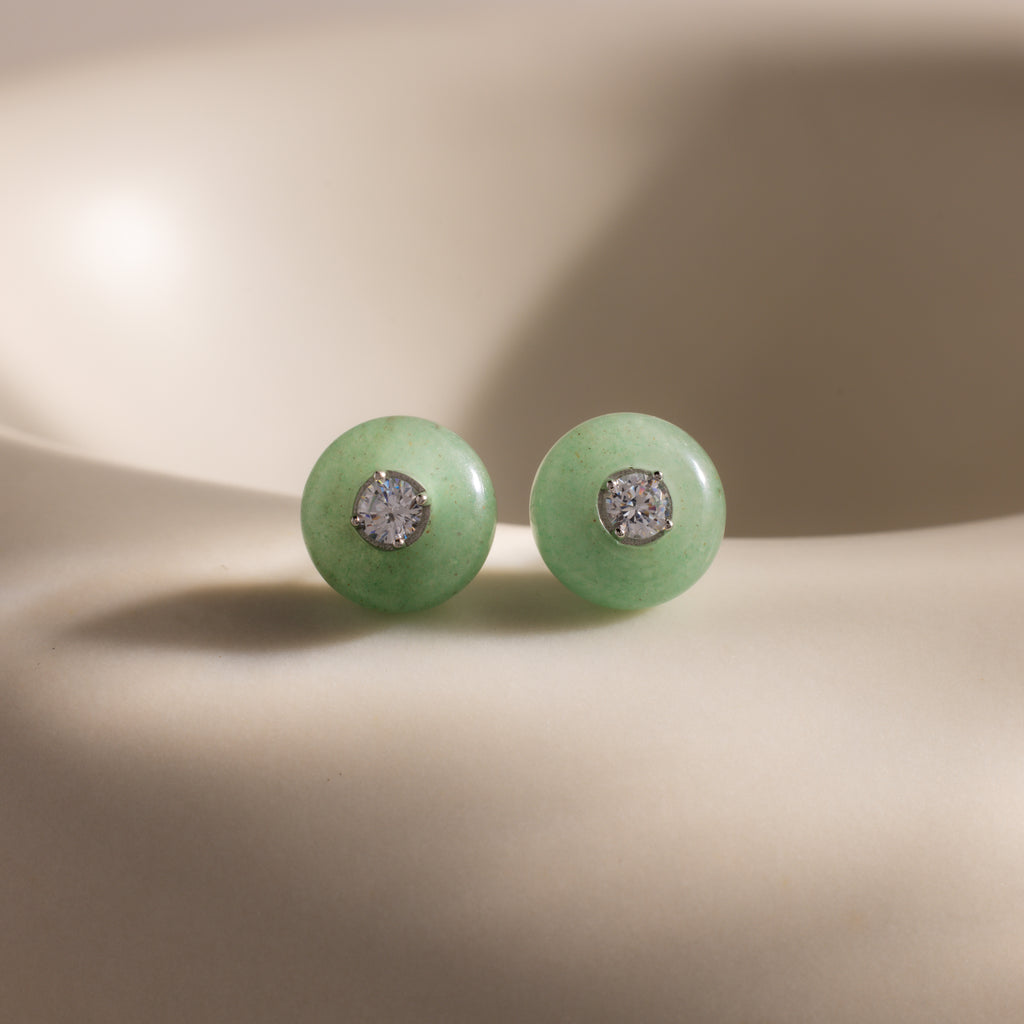 Close-up of round green jade stud earrings featuring a sparkling CZ diamond center and silver bezel setting, displayed on a neutral background.