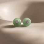 Close-up of round green jade stud earrings featuring a sparkling CZ diamond center and silver bezel setting, displayed on a neutral background.