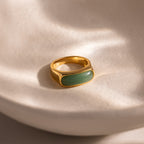 Close-up of a gold signet ring with a polished green jade gemstone inlay, displayed on a smooth ceramic dish.