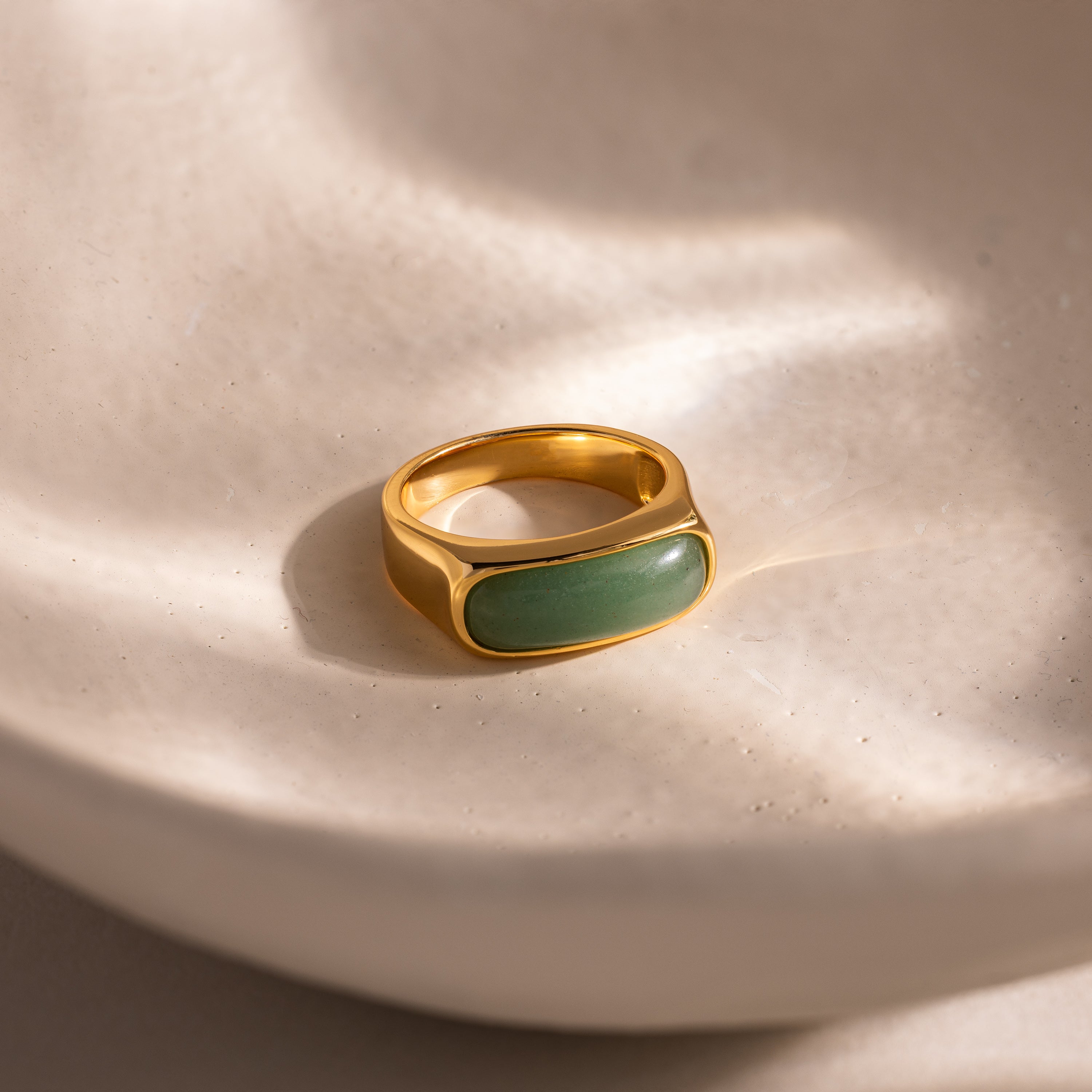 Close-up of a gold signet ring with a polished green jade gemstone inlay, displayed on a smooth ceramic dish.