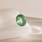 Thick green jade gemstone statement ring with a smooth, glossy finish, positioned upright on a white stone surface.