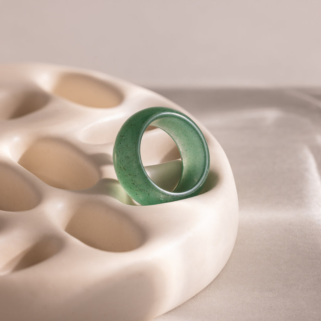 Thick green jade gemstone statement ring with a smooth, glossy finish, positioned upright on an off-white prop.