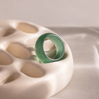 Thick green jade gemstone statement ring with a smooth, glossy finish, positioned upright on an off-white prop.