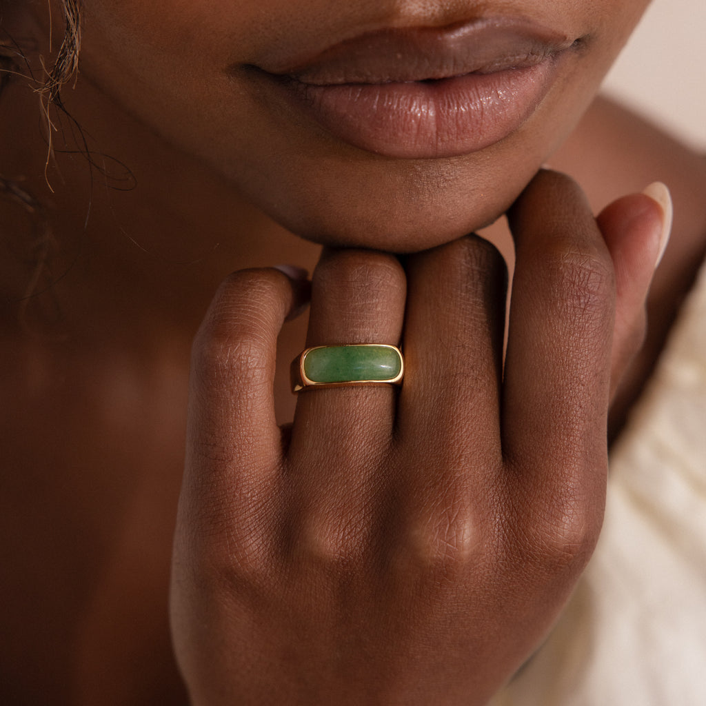 Model wearing a gold signet ring with a polished green jade gemstone inlay.