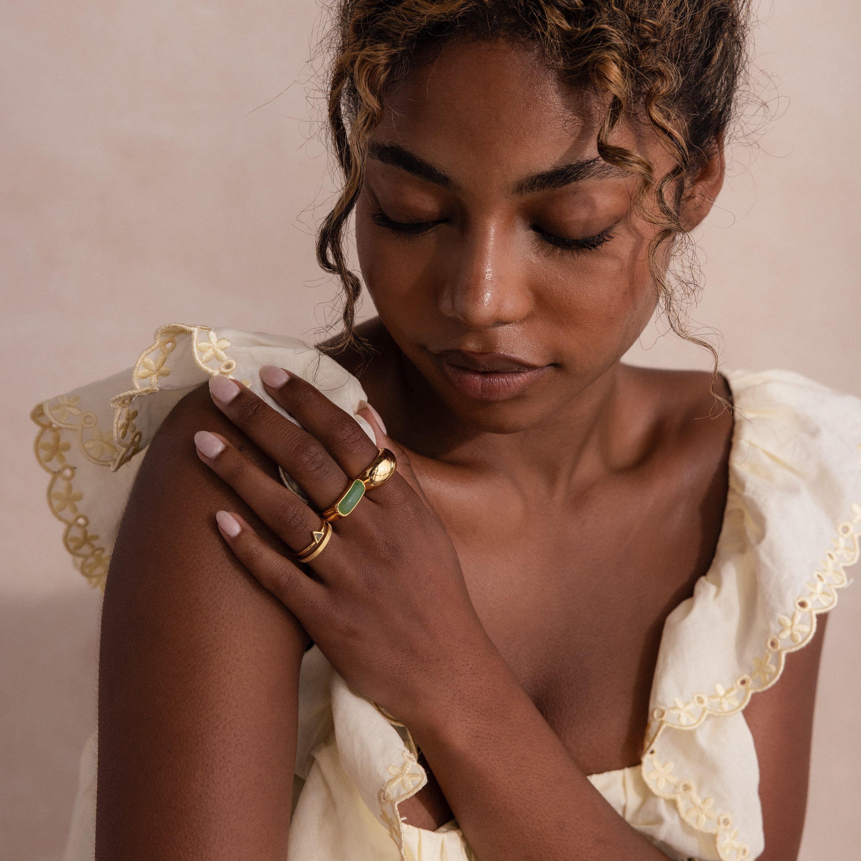 Model wearing a gold signet ring with a polished green jade gemstone inlay, stacked with multiple gold rings.