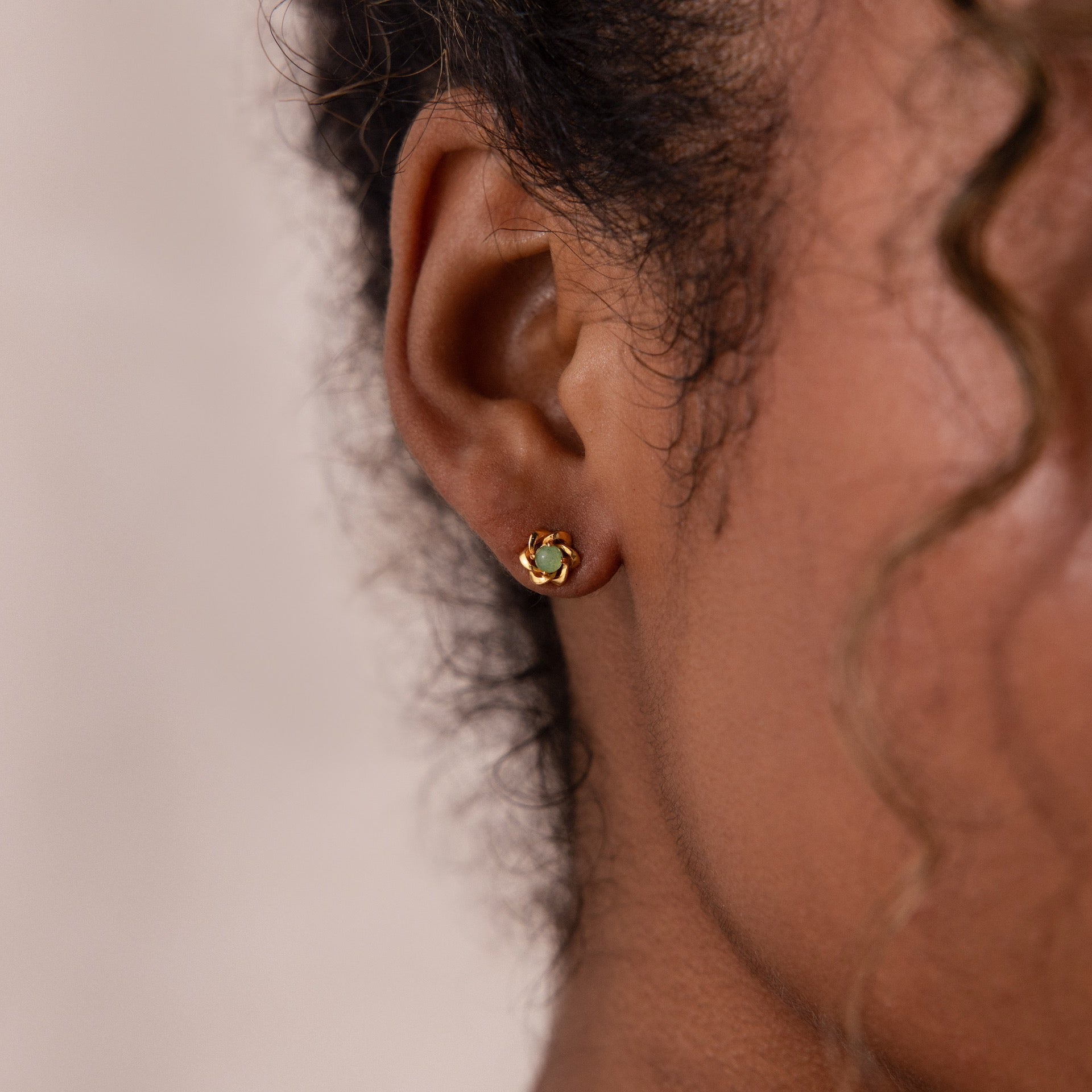 Up-close of model wearing a gold flower-shaped stud earring with a round green jade gemstone center.