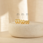 The Editor Huggie Earrings Set features four minimalist hoop earrings in increasing sizes, labeled Styles C, B, and A, displayed on a stone platform—perfect for any occasion.
