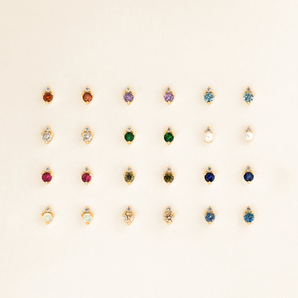 Twenty-five pairs of dainty earrings, including Raindrop Aquamarine Studs, are arranged in a neat grid on a light background.