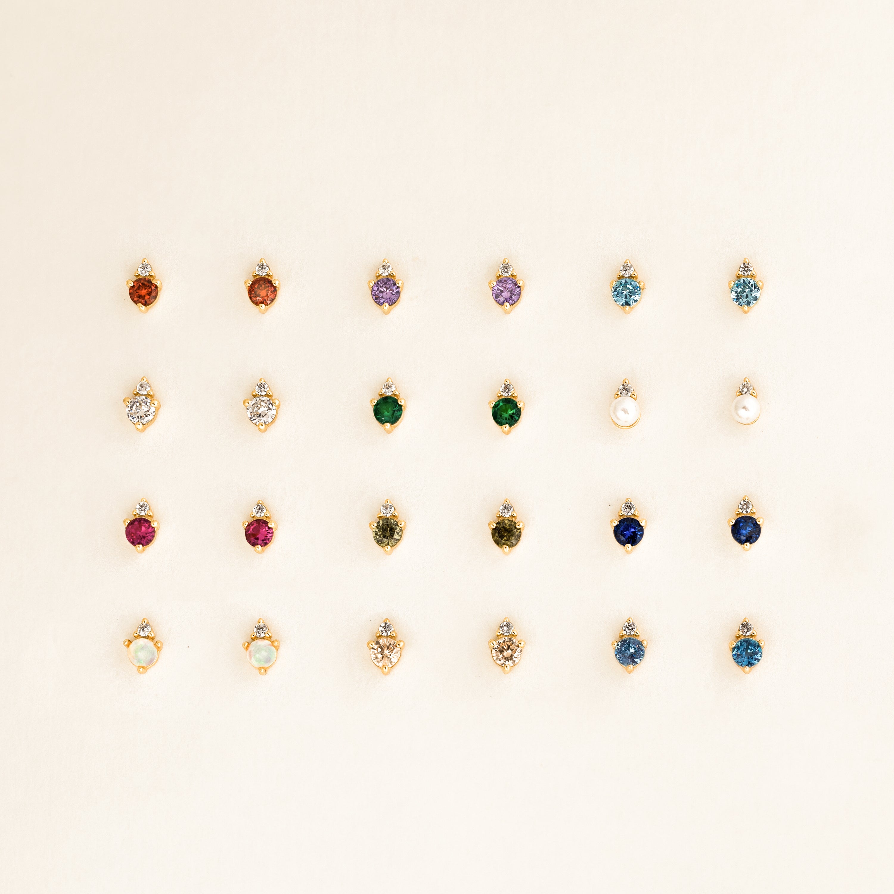 Twenty-five pairs of dainty earrings, including Raindrop Aquamarine Studs, are arranged in a neat grid on a light background.