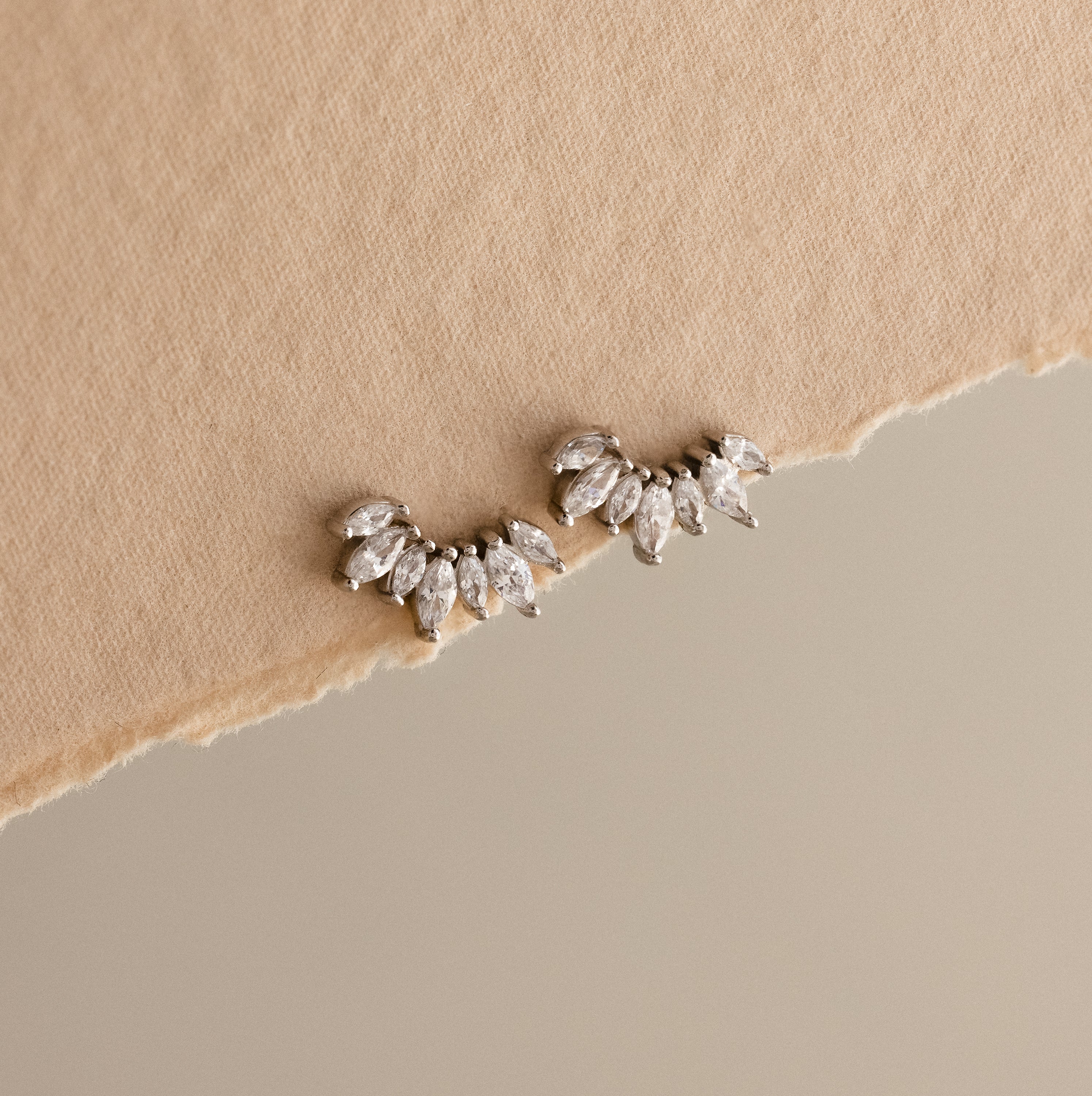 Marquise Diamond Arc Climbers in Silver, leaf-shaped ear climbers inspired by marquise diamonds, displayed on torn beige fabric with a neutral background.