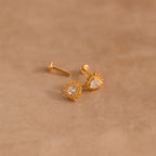 Sacred Heart Studs: gold earrings with clear gemstones and a delicate sunburst texture, displayed on a soft beige surface.