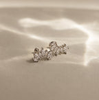 The Marquise Diamond Arc Climbers in Silver, featuring leaf-shaped marquise stones, are displayed on a soft beige surface with gentle light reflections.