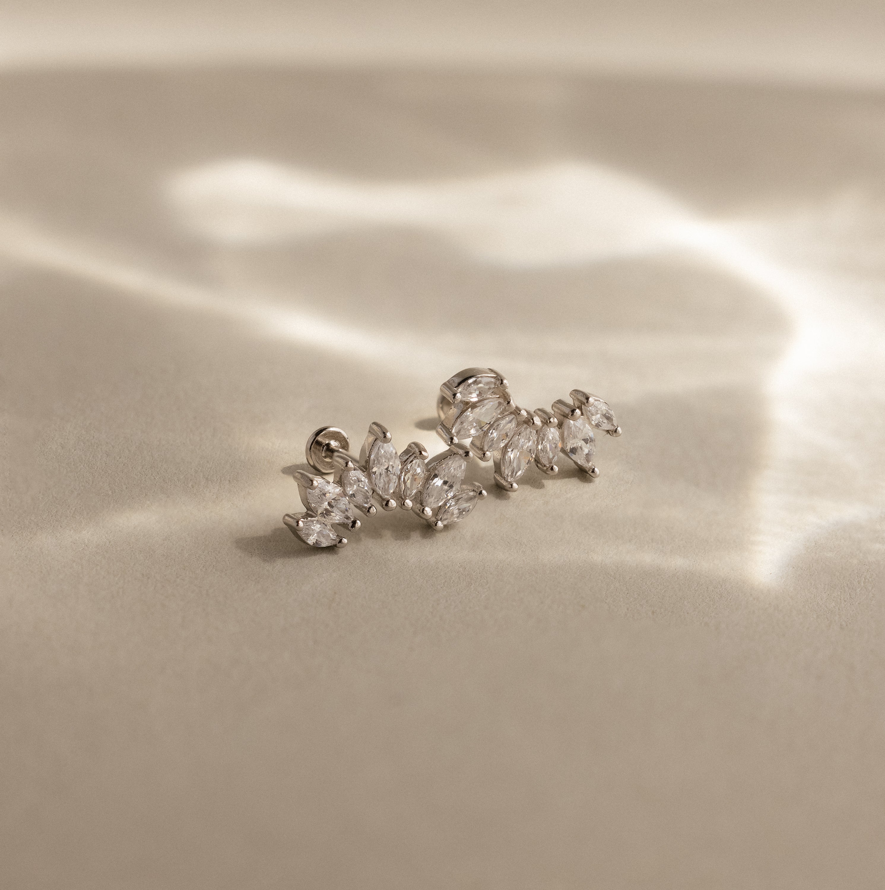 The Marquise Diamond Arc Climbers in Silver, featuring leaf-shaped marquise stones, are displayed on a soft beige surface with gentle light reflections.
