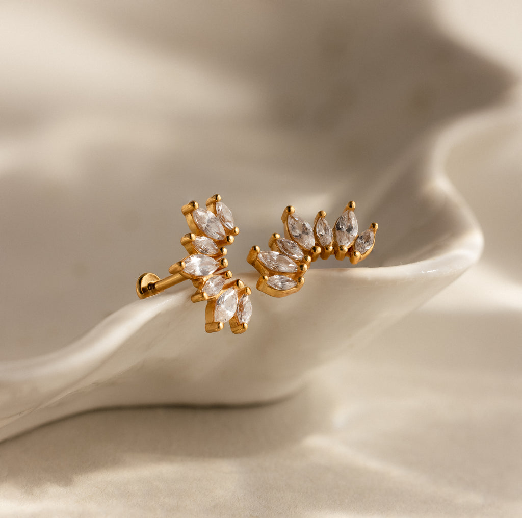 Marquise Diamond Arc Climbers in 18K Gold with marquise-cut clear stones, displayed on a wavy, cream-colored ceramic surface.