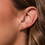 Close-up of a womans ear wearing Sacred Heart Studs featuring heart-shaped gemstones and a delicate sunburst texture.