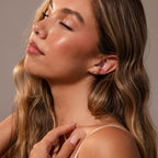 A woman with long, wavy hair and natural makeup showcases the Sacred Heart Studs, featuring a sunburst texture.