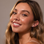 A woman with long wavy hair and glowing skin smiles at the camera, elegantly showcasing Marquise Diamond Arc Climbers in Silver against a neutral backdrop.