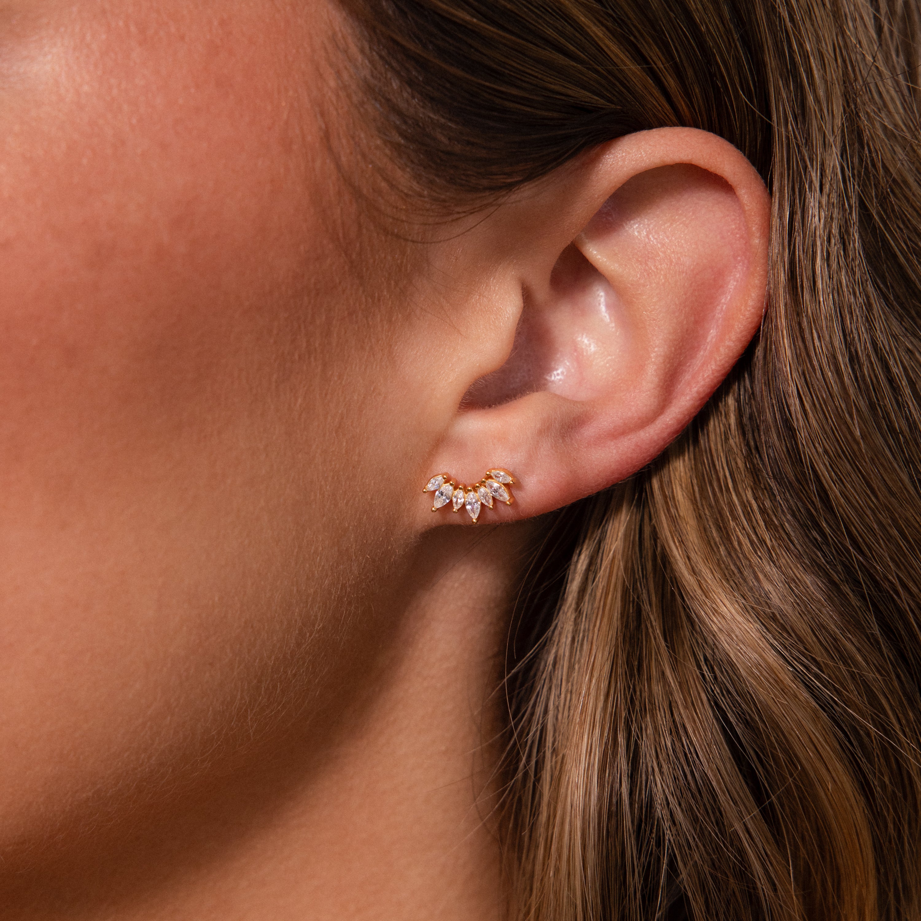 Close-up of a womans ear wearing Marquise Diamond Arc Climbers—delicate gold earrings with sparkling marquise-shaped stones.