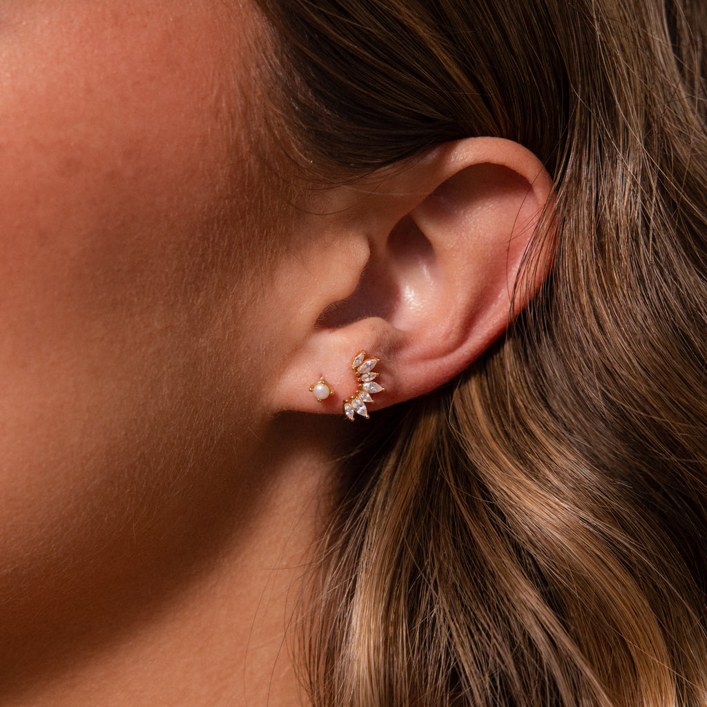 Close-up of a womans ear with delicate earrings: a small pearl stud and our Marquise Diamond Arc Climbers adorned with sparkling marquise stones.