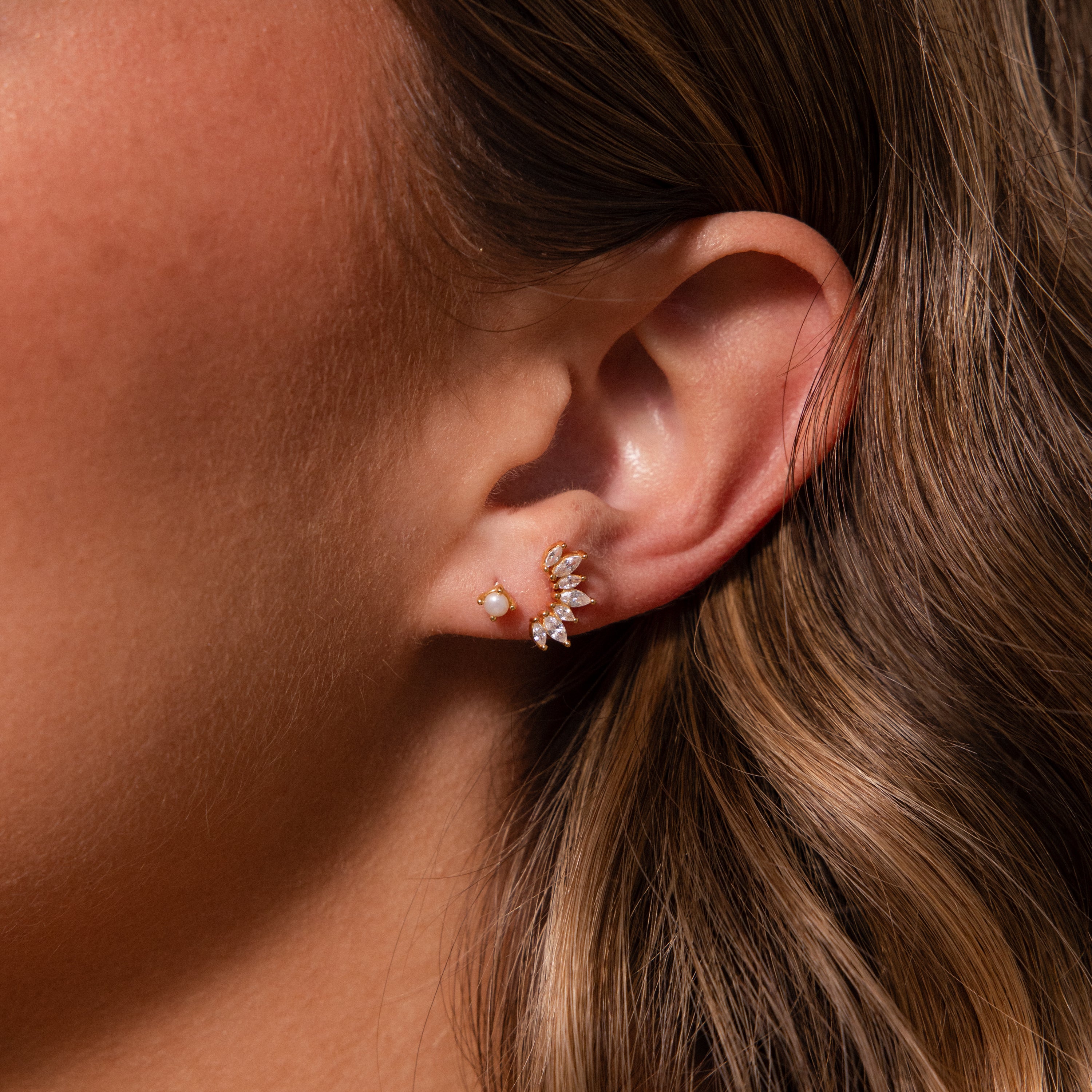 Close-up of a womans ear with delicate earrings: a small pearl stud and our Marquise Diamond Arc Climbers adorned with sparkling marquise stones.