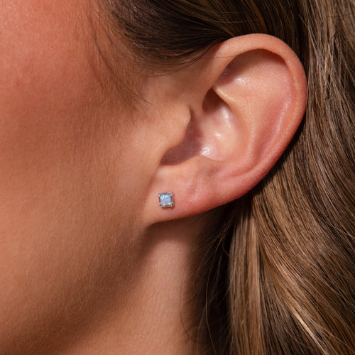 Close-up of a womans ear with light brown hair, wearing our Blue Opal Prism Studs in Silver—ideal for lovers of iridescent jewelry.