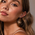 A close-up of a young woman with wavy brown hair, glowing skin, and delicate Blue Opal Prism Studs in Silver that add a touch of iridescent beauty.
