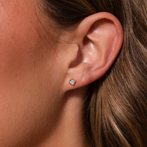 Close-up of a woman’s ear wearing Blue Opal Prism Studs in 18K Gold—small, iridescent square blue opal earrings set in delicate gold.