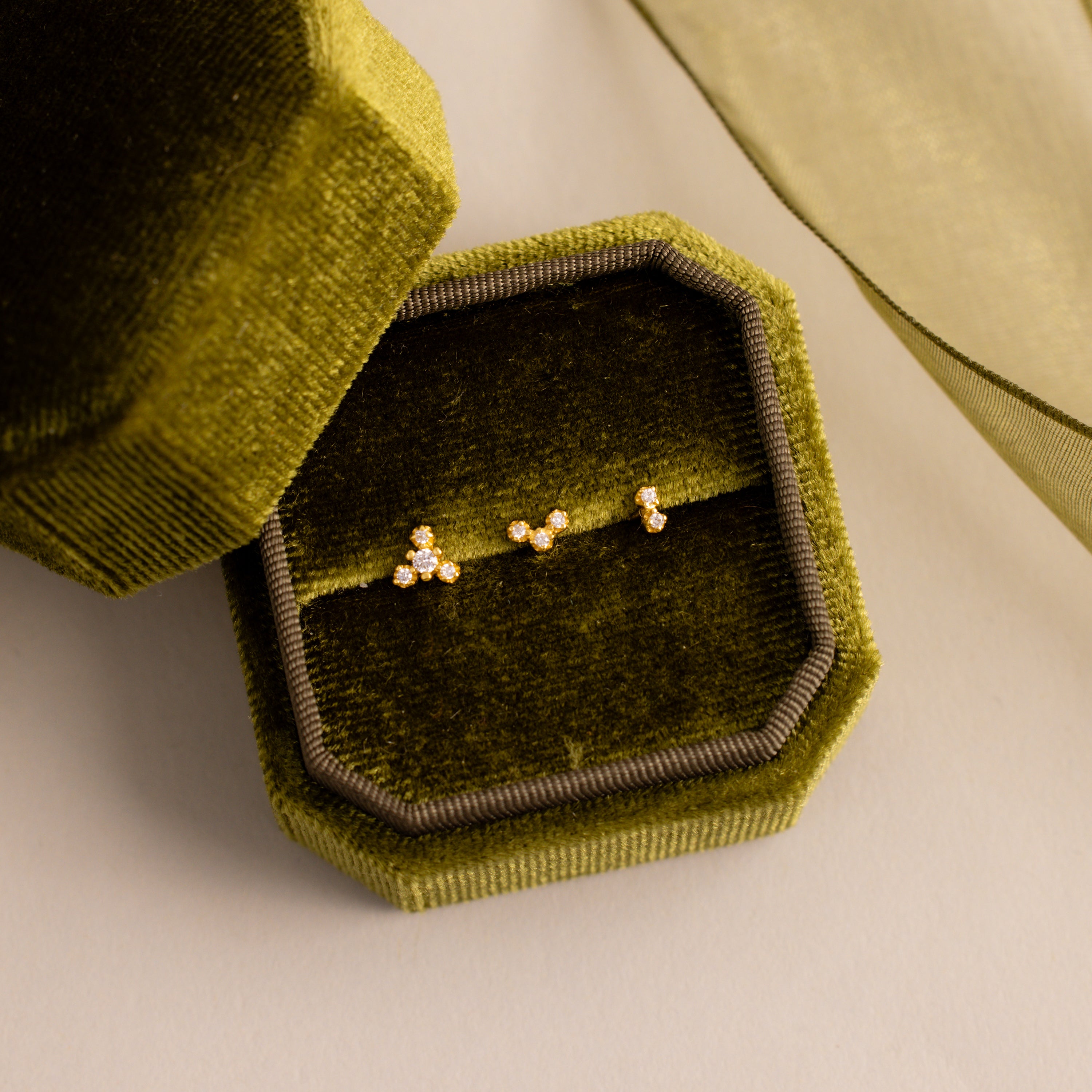 Three dainty crystal cluster flat back stud earrings in gold displayed inside an olive green velvet jewelry box.