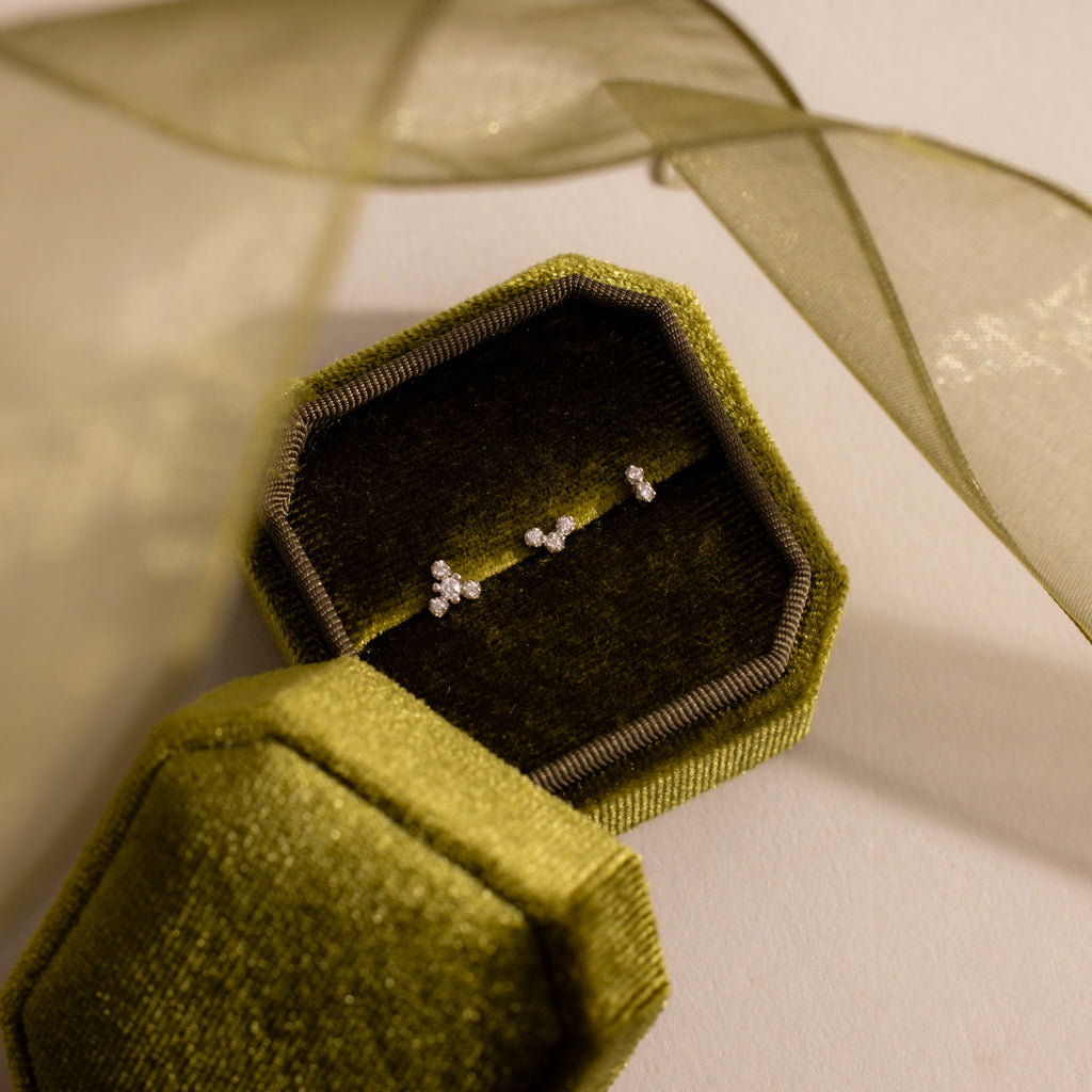 Three dainty crystal cluster flat back stud earrings in silver displayed inside an olive green velvet jewelry box.