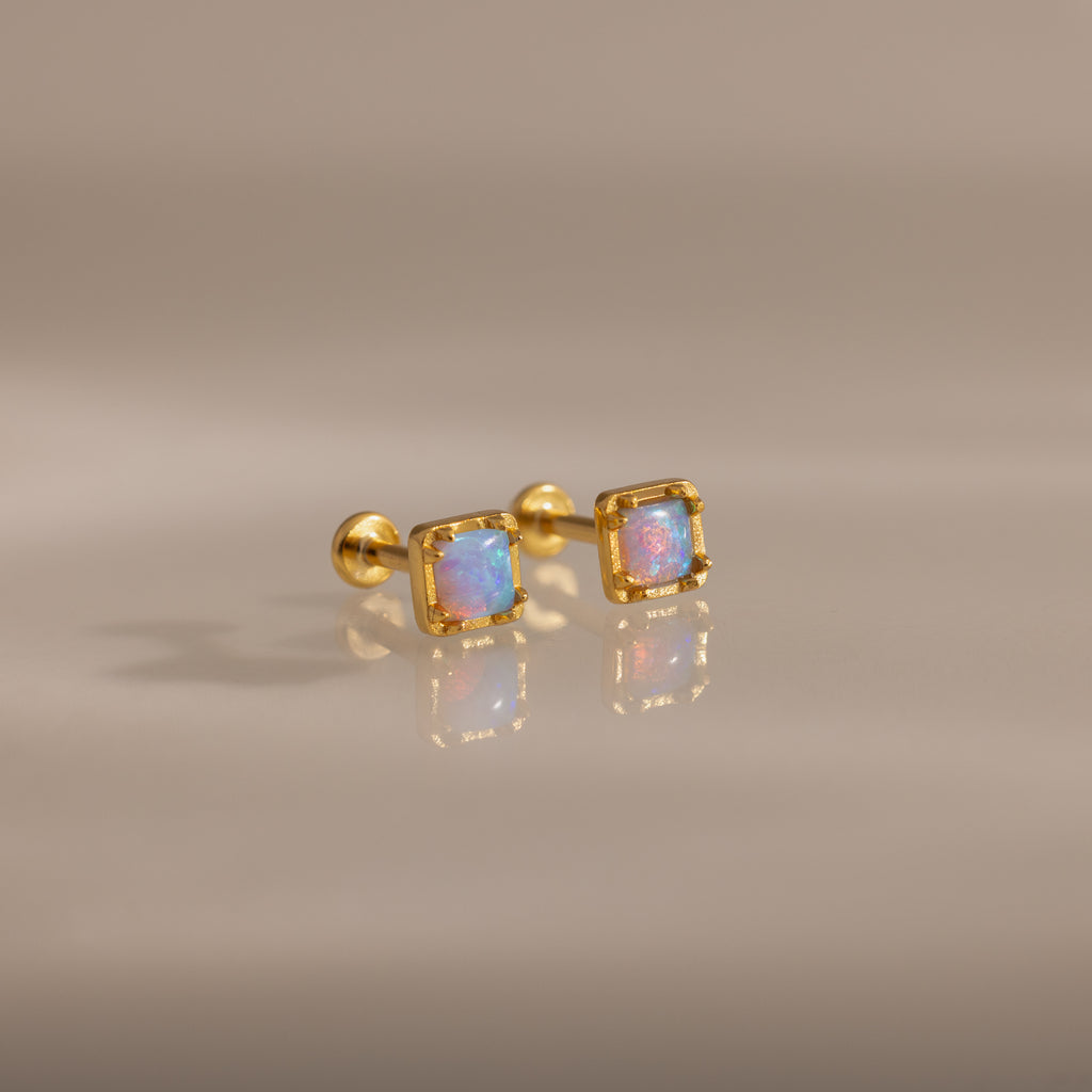 Blue Opal Prism Studs in 18K Gold featuring square blue opals, showcased on a smooth, reflective surface.