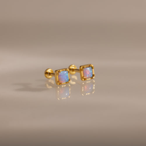 Blue Opal Prism Studs in 18K Gold featuring square blue opals, showcased on a smooth, reflective surface.