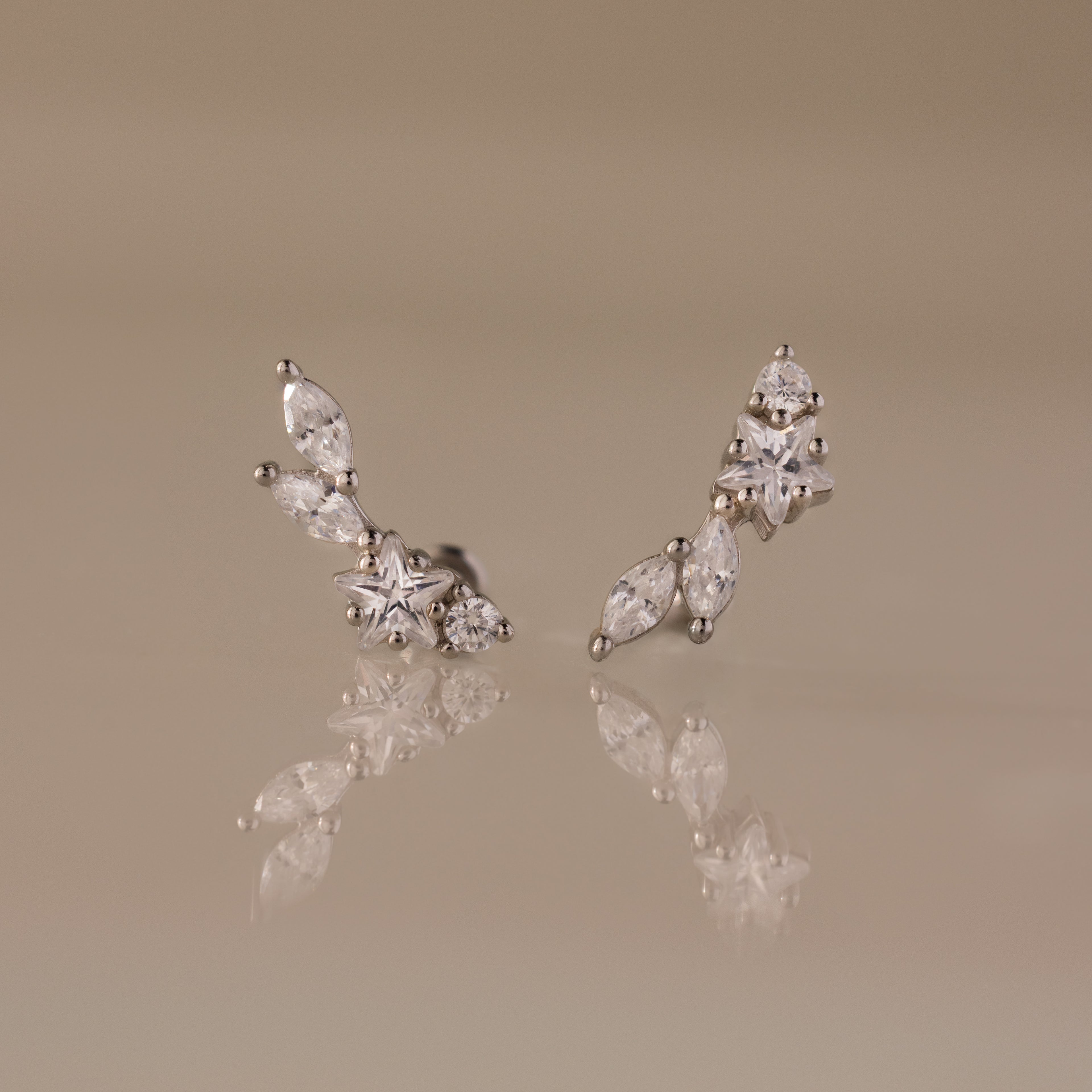 Diamond Starfall Climbers in Silver, featuring marquise and round white gemstones, styled as elegant ear climbers, displayed on a glossy beige surface.