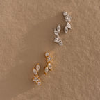 A pair of Diamond Starfall Climbers, gold earrings with star accents, displayed on a textured beige surface.