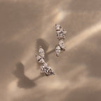 The Diamond Starfall Climbers in Silver, featuring marquise cuts with delicate leaf and star designs, rest on a beige surface bathed in soft light and shadows for an elegant effect.