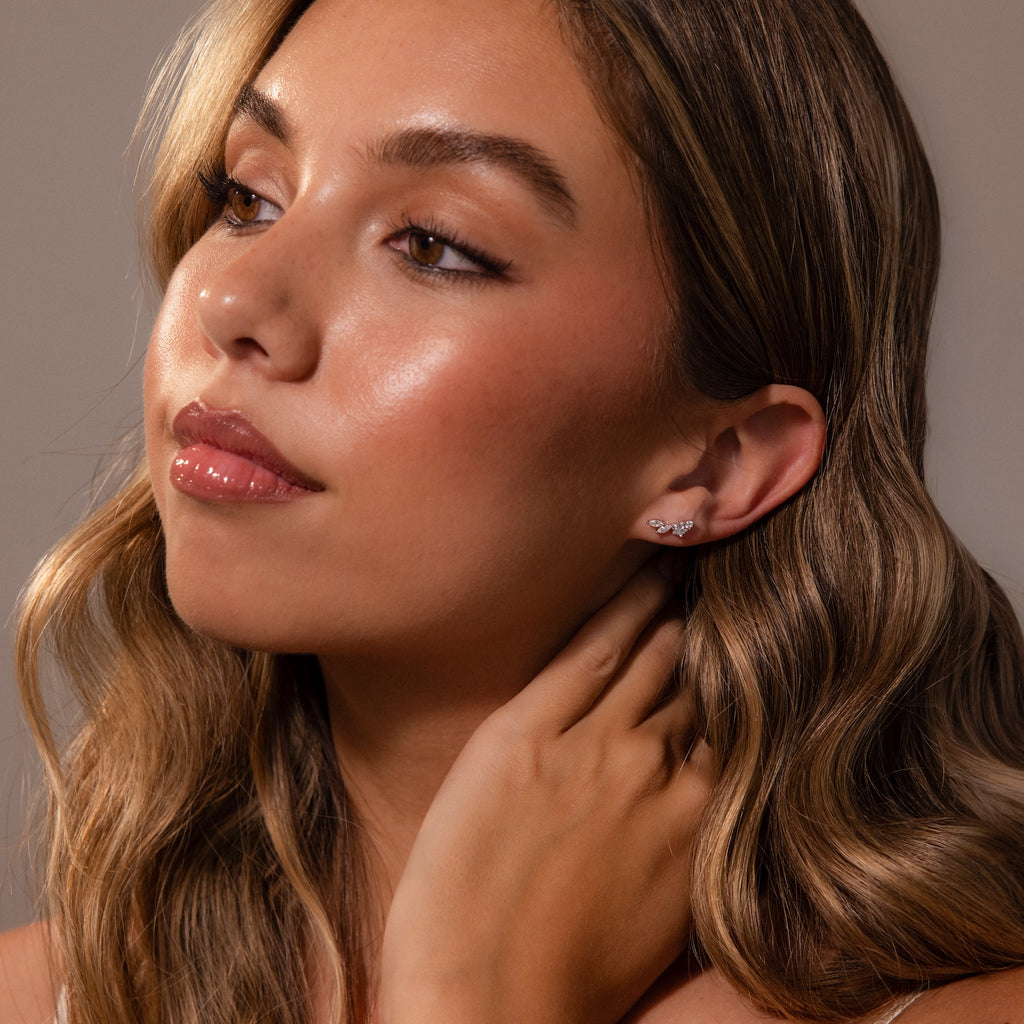 Woman with wavy hair touches her neck and looks to the side, wearing Diamond Starfall Climbers in Silver.