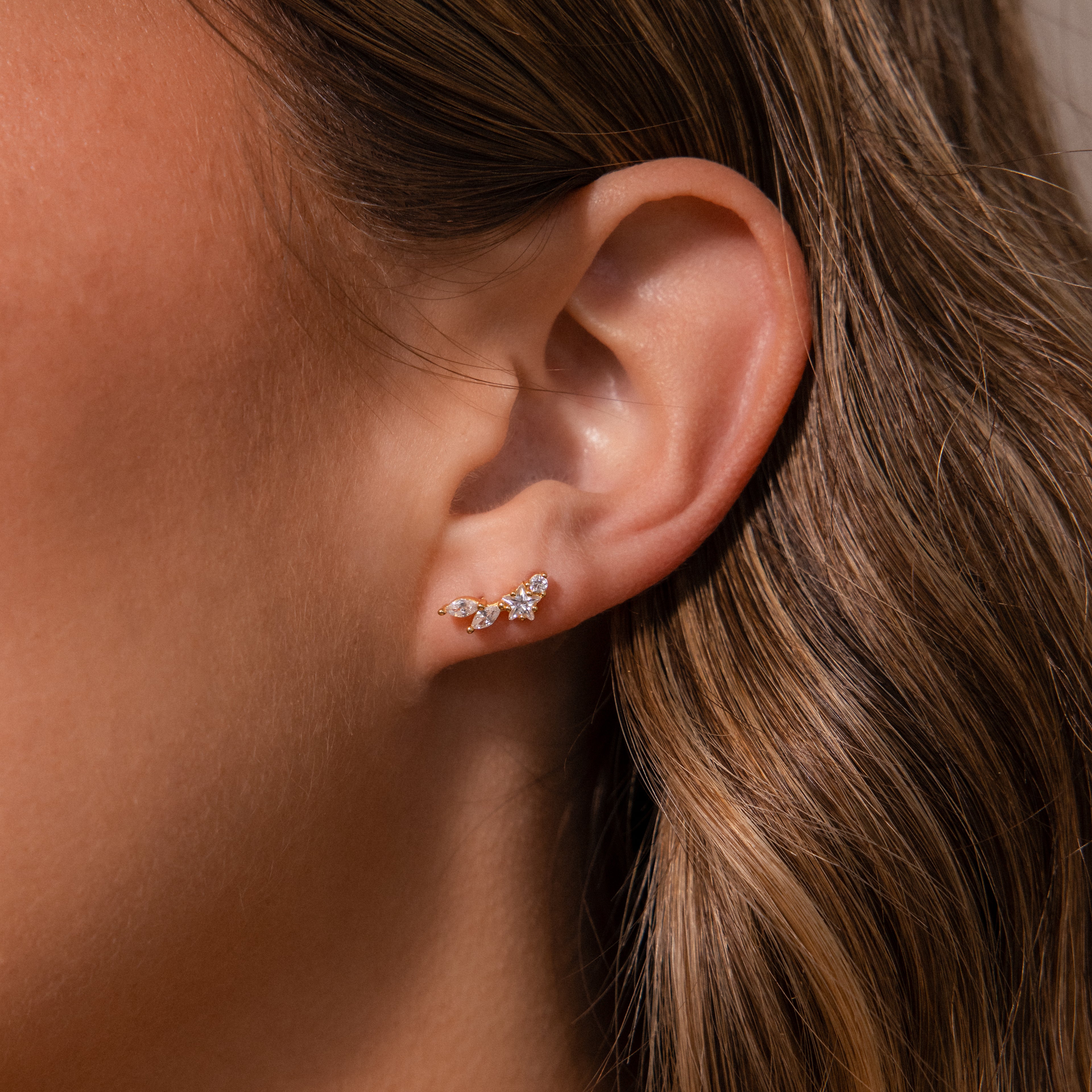 Close-up of an ear wearing Diamond Starfall Climbers, showcasing marquise cut stones and a subtle star accent in their elegant curved gold design.