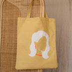 Yellow tote bag with a minimalist woman’s face, white hair, and orange earring and necklace—ideal for unique style lovers. Get a Free Gift of Choice with your purchase!.