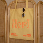 Brighten your day with the Free Gift of Choice—a yellow tote bag featuring "Her!" in orange text and sunglasses detail, making it a perfect pick for tote bag lovers or as a cheerful free gift.