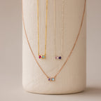 The Toi et Moi Infinity Heart Birthstone Necklaces, featuring colorful gemstone pendants, are displayed on a textured white vase—perfect for adding a personal touch to any look.