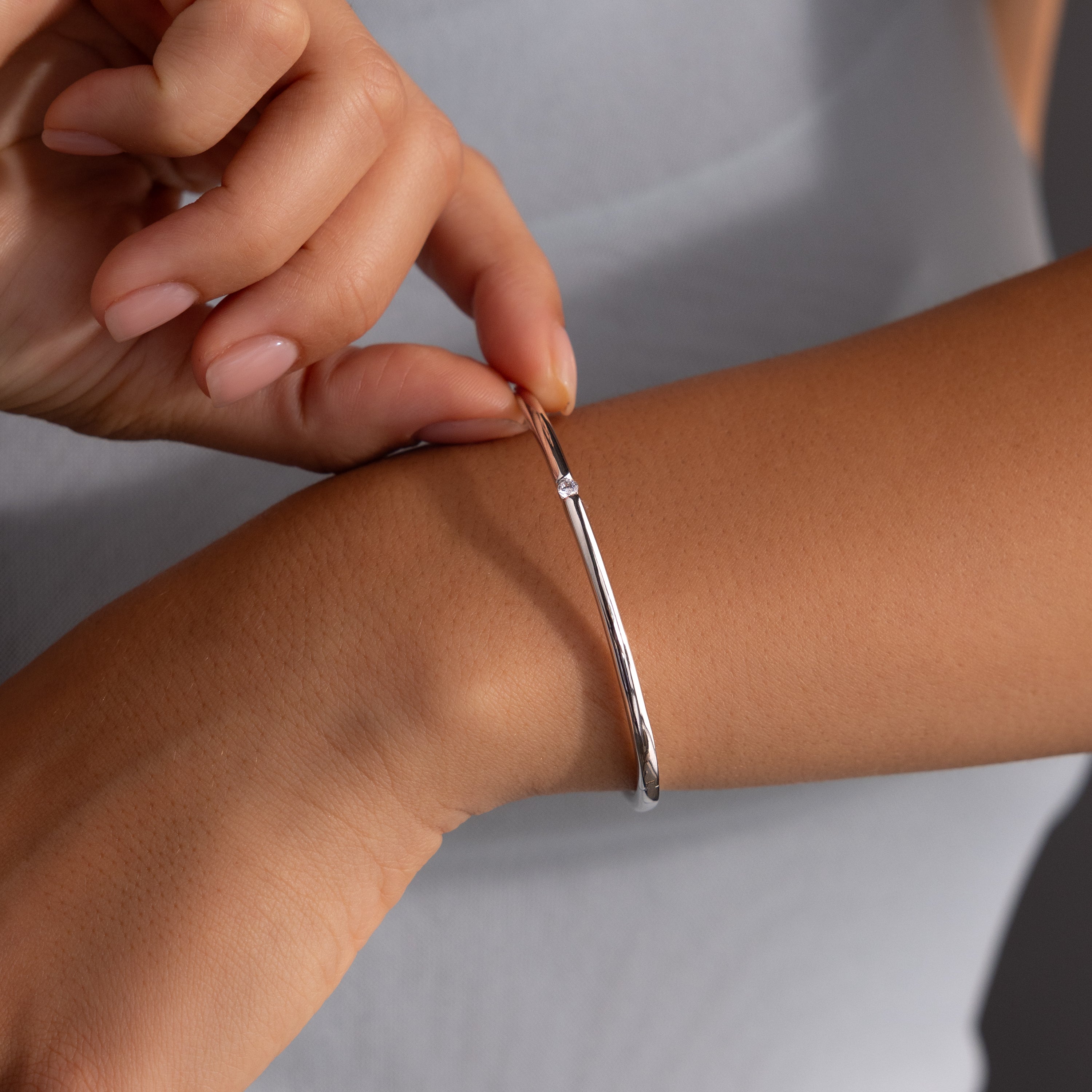Someone slips on the Skinny Diamond Bangle in White Gold, pairing its minimalist sparkle with a light grey sleeveless top.