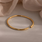 The Skinny Diamond Bangle in 18K Gold, adorned with sparkling stones, rests elegantly on a soft beige fabric background.