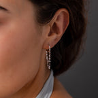 Close-up of a woman's ear wearing Duo Mirror Chain Huggies in Sterling Silver, featuring small dangling beads, set against a dark background—an elegant display of modern jewelry.