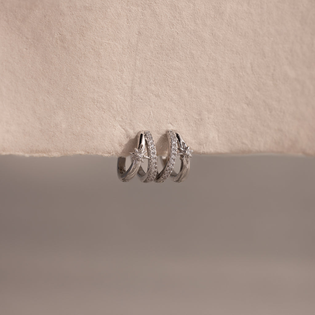 The Starburst Pave Duo Huggies in Sterling Silver rest on a textured, off-white surface, perfect for pairing with silver rings or gold hoops for a celestial-inspired look.