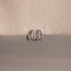 The Starburst Pave Duo Huggies in Sterling Silver rest on a textured, off-white surface, perfect for pairing with silver rings or gold hoops for a celestial-inspired look.